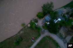 The roaring Yellowstone River is seen from the air sweeping over trees and near homes Tuesday, June 14, 2022, in Billings, Mont. (AP Photo/Brittany Peterson)