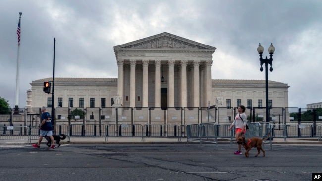 People walk dogs past anti-scaling fencing erected around the U.S. Supreme Court in Washington, June 23, 2022. (AP Photo/Gemunu Amarasinghe)