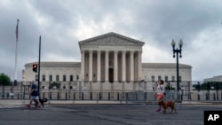 People walk dogs past anti-scaling fencing erected around the U.S. Supreme Court in Washington, June 23, 2022.