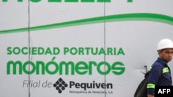 ARCHIVO - Un trabajador camina cerca de una valla con el logo de Monómeros en Barranquilla, Colombia, el 9 de octubre de 2021.