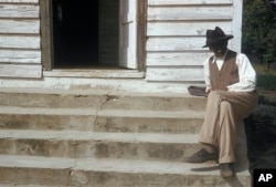 Seorang pria yang ikut dalam studi sifilis tahun 1950-an, duduk di tangga di depan sebuah rumah di Tuskegee, Alabama. (Arsip Nasional via AP)