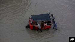 Orang-orang mendorong bajaj di jalan yang tergenang banjir setelah hujan lebat di Karachi, Pakistan, 7 Juli 2020.