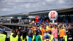 Unjuk rasa serikat pekerja Prancis di luar terminal bandara Roissy, utara Paris, Jumat, 1 Juli 2022. (AP Photo/ Thomas Padilla)