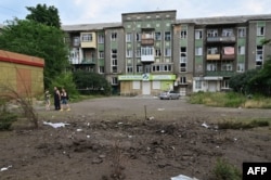 People check a crater left by a bomb dropped July 5, 2022, in a residential neighborhood of Sloviansk, Donetsk province, damaging nearby buildings.
