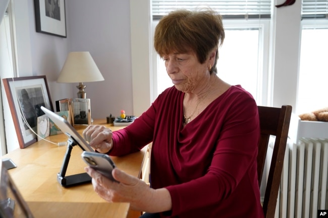 Pat Olken, of Sharon, Mass., demonstrates using the Otter app on her iPhone while using an iPad at her home, in Sharon, Thursday, April 14, 2022.(AP Photo/Steven Senne)