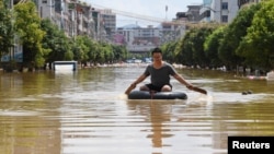 中国广东英德洪水泛滥的街头，一名男子划着一个轮胎过街。（2022年6月23日）