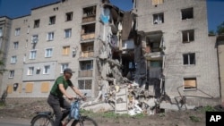 A man rides a bicycle past a building damaged in Russian shelling in Bakhmut, Donetsk region, Ukraine, Monday, June 20, 2022. 