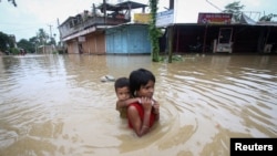 Seorang gadis menggendong adiknya saat dia mengarungi jalan yang banjir setelah hujan lebat, di pinggiran Agartala, India, 18 Juni 2022. Pada 6 September 2022, Bengaluru, India Selatan juga mengalami banjir setelah dua hari diguyur hujan deras.(Foto: REUTERS/Jayanta Dey)