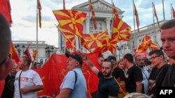 Supporters of North Macedonia's main opposition party VMRO-DPMNE wave party flags and national flags as they march during a rally in front of a government building in Skopje, June 18, 2022