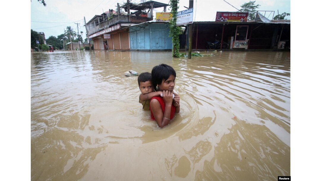 Seorang anak perempuan menggendong adiknya saat mengarungi jalan yang terendam banjir setelah hujan lebat, di pinggiran Agartala, India, 18 Juni 2022. (REUTERS/Jayanta Dey)