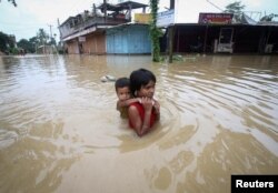 Seorang anak perempuan menggendong adiknya saat mengarungi jalan yang terendam banjir setelah hujan lebat, di pinggiran Agartala, India, 18 Juni 2022. (REUTERS/Jayanta Dey)