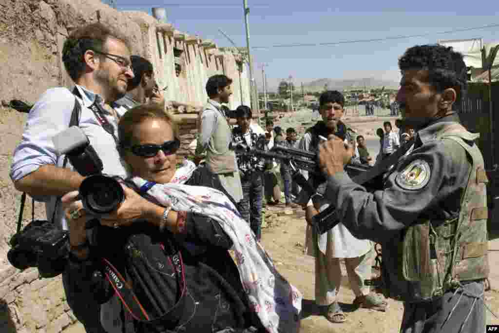 Un policía afgano apunta con su arma a los fotoperiodistas Paula Bronstein y Kevin Frayer mientras les impide acercarse al área donde tres hombres armados asaltaron un banco en Kabul el 19 de agosto de 2009.&nbsp;