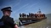 aqZSeorang polisi Inggris berjaga di Pantai Dungeness di tenggara pantai Inggris ketika rekannya membantu para migran yang dievakuasi dari Selat Inggris saat mencoba menyeberangi selat itu dari Perancis, 15 Juni 2022 (Foto: Ben Stansall / AFP)