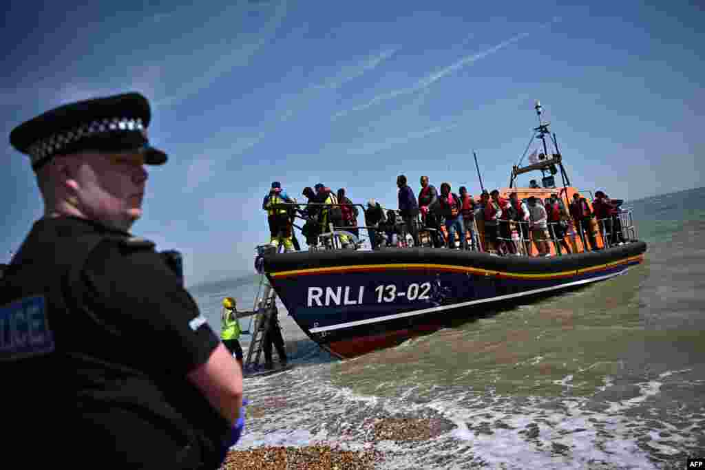 A British police officer stands guard on the beach of Dungeness, on the southeast coast of England, as Royal National Lifeboat Institution&#39;s staff members help migrants disembark from a lifeboat after they were picked up at sea while attempting to cross the English Channel.&nbsp;