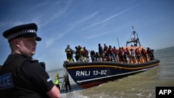 FILE: A British policeman on the beach of Dungeness, on the southeast coast of England, as Royal National Lifeboat Institution's staff members help migrants disembark from a lifeboat after they were picked up at sea while attempting to cross the English Channel, June 15, 2022