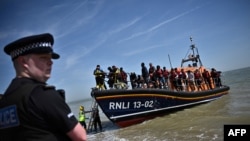 FILE - A British police officer stands guard on the beach of Dungeness, on the southeast coast of England, on June 15, 2022, as migrants disembark from a lifeboat after they were picked up at sea while attempting to cross the English Channel.