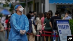 A worker in protective gears reacts as residents line up at a testing site due to requirements for a negative COVID test in the last 72 hours to enter some buildings and using public transportation in Beijing, China, July 4, 2022. 