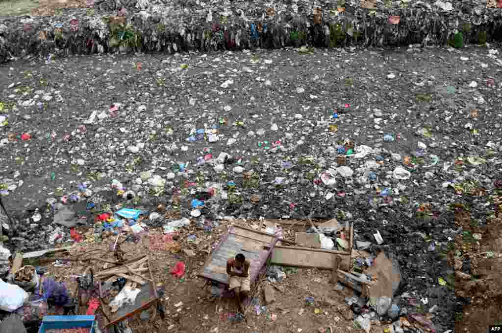 A man sits on a cart next to a sewer canal filled with plastic and other waste in New Delhi, India.