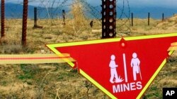 FILE - An international sign warning about mines hangs beside a minefield at Bagram Air Base on, March 22, 2002.