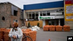 FILE - A woman stands near bricks used to rebuild a building in Makariv, on the outskirts of Kyiv, Ukraine, May 27, 2022.