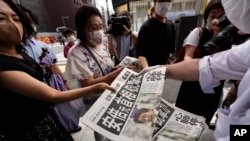 An employee distributes extra editions of the Yomiuri Shimbun newspaper reporting on Japan's former Prime Minister Shinzo Abe was shot, July 8, 2022, in Tokyo.
