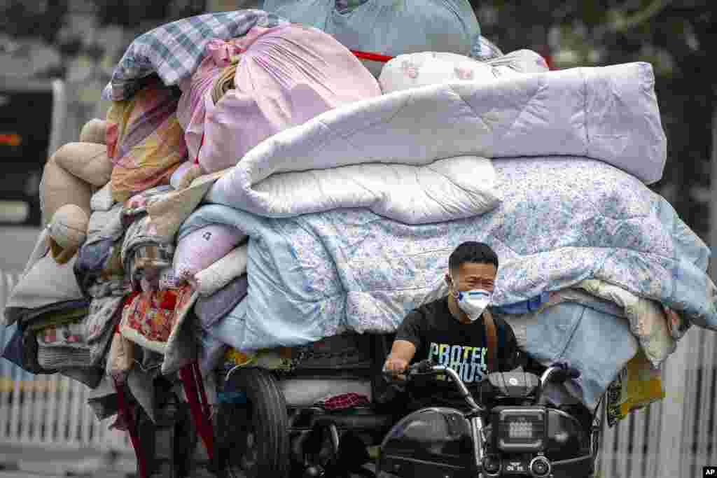 A man wearing a face covering drives a cart loaded with bedding and fabric along a street in Beijing, China.