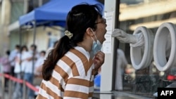A health worker takes a sample from a woman to be tested for COVID-19 at a swab collection site in Beijing, July 6, 2022.