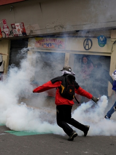 Un manifestante sostiene un bote de gas lacrimógeno durante un enfrentamiento con personal de seguridad.