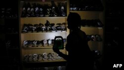 FILE: In this photo taken on February 16, 2022 A woman uses a rechargeable LED lantern to illuminate a shoe rack while shopping at the Sinnoville Centre after its electricity supply was cut off.