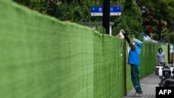 A delivery worker passes an order over the fence on a street in a residential area under a Covid-19 lockdown in Shanghai's Huangpu district on June 22, 2022.