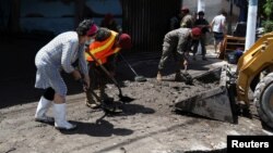 A woman and soldiers clean mud from the street after a flood caused by heavy rain in the aftermath of what is now known as Hurricane Bonnie, in Ilopango, El Salvador, July 3, 2022. 