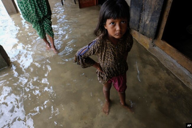 A girl reacts to camera as family members inspect their damaged belongings at her home, Wednesday, June 22, 2022. (AP Photo/Mahmud Hossain Opu)