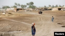 Seorang perempuan berjalan untuk mengambil air dari pompa tangan terdekat dengan pendingin air di kepalanya, saatgelombang panas, di pinggiran Jacobabad, Pakistan, 16 Mei 2022. (REUTERS/Akhtar Soomro)