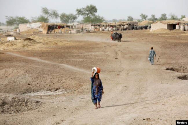 A woman walks to fetch water from a nearby hand-pump with a water cooler on her head, during a heatwave, on the outskirts of Jacobabad, Pakistan, May 16, 2022. (REUTERS/Akhtar Soomro)