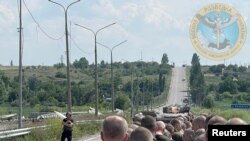 Seorang pria yang memegang bendera putih mengawasi proses pertukaran tawanan perang antara Rusia dan Ukraina di wilayah Zaporizhzhia, dalam foto yang dirilis pada 29 Juni 2022. (Foto: Ukraine's Military Intelligence/Handout via Reuters)