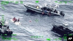 FILE - This photo released by the Seventh U.S. Coast Guard District shows people standing on a capsized boat, left, as some of its passengers are pulled up on to a rescue boat, top, in the open waters northwest of Puerto Rico, May 12, 2022. Haiti has gone into freefall as violence soars and the economy tumbles, forcing many Haitians into making potentially deadly voyages aboard rickety boats.