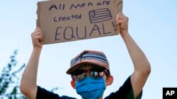 FILE - A boy holds a sign saying "All men are created equal," as he attends a protest on June 7, 2020, near the White House in Washington, over the death of George Floyd, a black man who was in police custody in Minneapolis. 