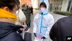 A worker wearing a protective suit holds a paper with a QR code for the Beijing health code app at a private coronavirus testing site in Beijing, Jan. 26, 2022. 