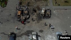 People stand next to cars destroyed by a Russian missile strike at a residential area in Kharkiv, Ukraine, June 26, 2022. 