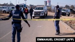 FILE — South African Police Service (SAPS) officers enforce a perimeter around a crime scene as pathalogical investigators inspect the crime scene where 14 people where shot dead in a tavern, in Soweto, on July 10, 2022. 