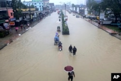 People wade through flooded waters in Sylhet, Bangladesh, June 18, 2022. At least 18 people have died as floods cut a swatch across northeastern India and Bangladesh, leaving millions of homes underwater.