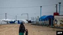 FILE - This file photo taken on March 4, 2021 shows a woman holds a child's hand as they stand in the rain at Camp Roj, where relatives of people suspected of belonging to the Islamic State (IS) group are held, near al-Malikiyah (Derik) in Syria's northea