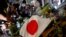 A Japanese flag is seen as people pray next to tributes laid at the site where late former Japanese Prime Minister Shinzo Abe was shot while campaigning for a parliamentary election, near Yamato-Saidaiji station in Nara, western Japan, July 8, 2022.