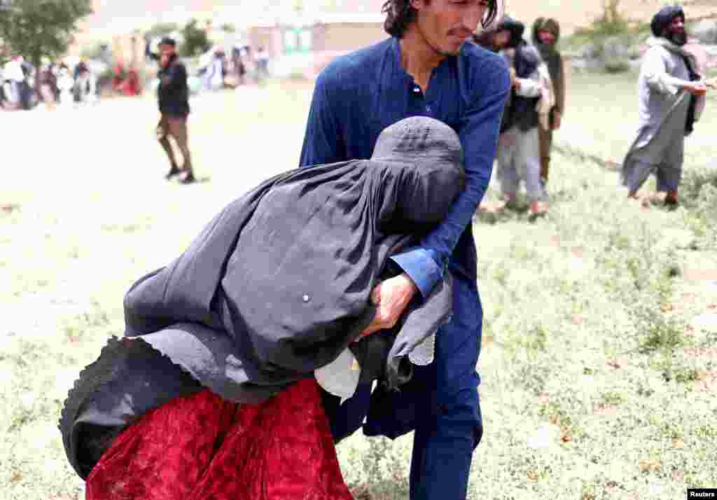 An Afghan woman is helped to reach an evacuation helicopter after she lost some of her relatives in an earthquake in Gayan, Afghanistan