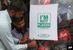 Pekerja toko helm menempelkan bahan pengganti plastik yang dapat terurai pada kaca di Hyderabad, India, Kamis, 30 Juni 2022. (AP/Mahesh Kumar A.)