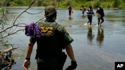 FILE - A Border Patrol agent watches as a group of migrants walk across the Rio Grande on their way to turn themselves in upon crossing the U.S.-Mexico border, June 15, 2021, in Del Rio, Texas.