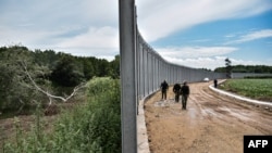 FILE - Police officers patrol along a steel fence along the Evros river, Greece's river border with Turkey, near the village of Poros, June 8, 2021. 