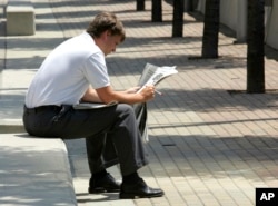 FILE - A man reads a newspaper during his lunch break in Cincinnati on July 6, 2005. A report from Northwestern University says local newspapers in the United States are dying at the rate of two per week.