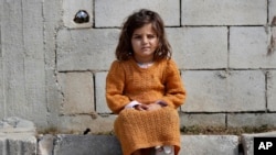 FILE - A displaced Syrian girl sits outside her family's tent at a refugee camp in Bar Elias, Bekaa Valley, Lebanon, March 5, 2021. 