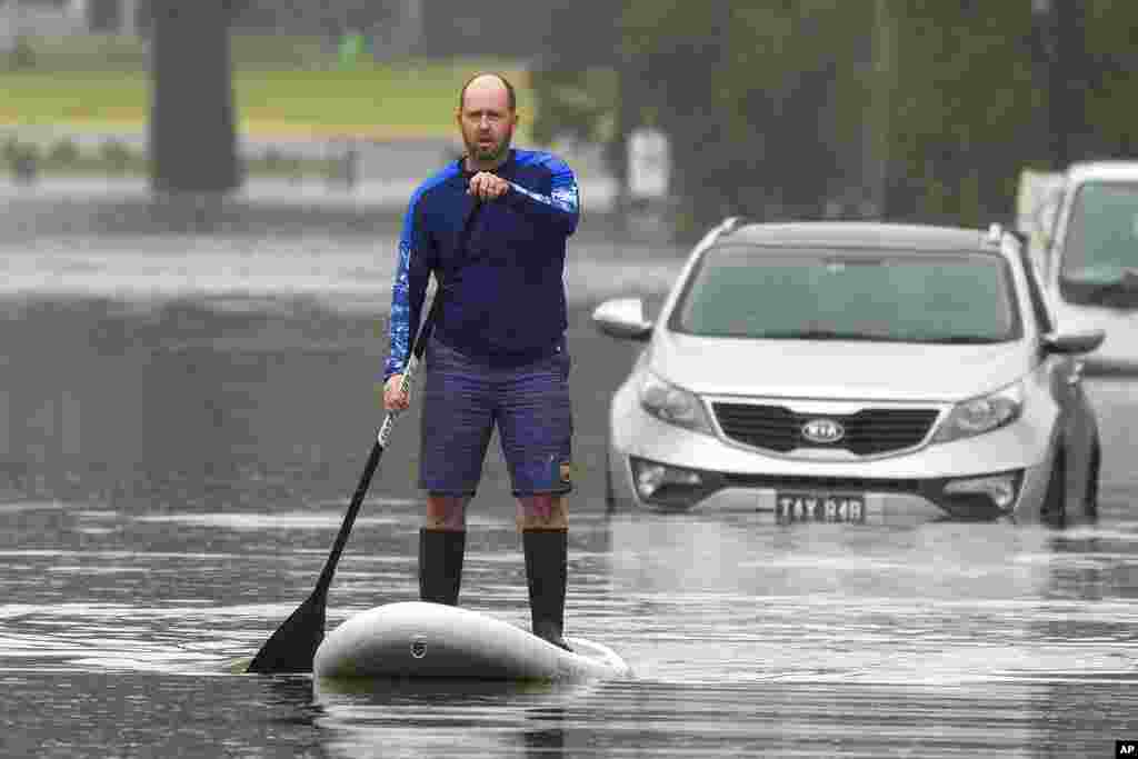 A man paddles on a stand-up paddle board through a flooded street at Windsor on the outskirts of Sydney, Australia.